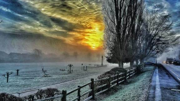 A frosty park landscape with sun piercing through the clouds.