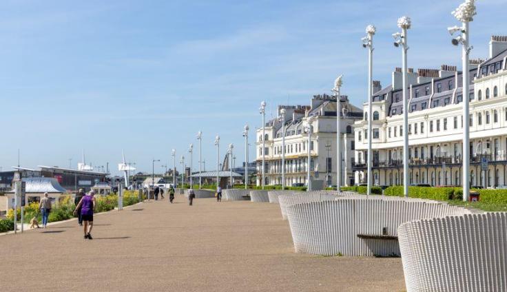 Dover seafront, a yellow stony path with tall white buildings on the right and blue sky.