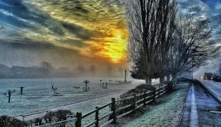 A frosty park landscape with sun piercing through the clouds.
