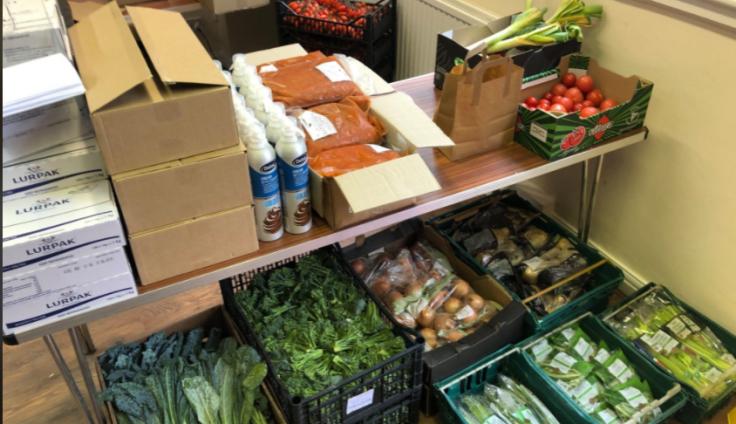 Produce in boxes and crates stacked on a table and the floor, ready to be distributed.