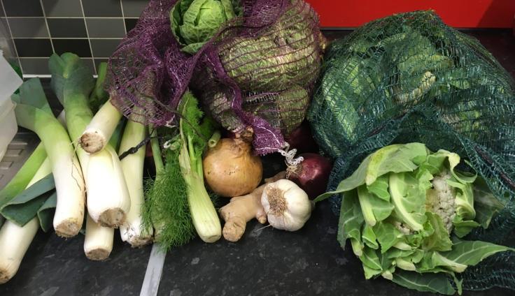 Pile of different vegetables on a grey kitchen counter, including leeks, cabbage and garlic.