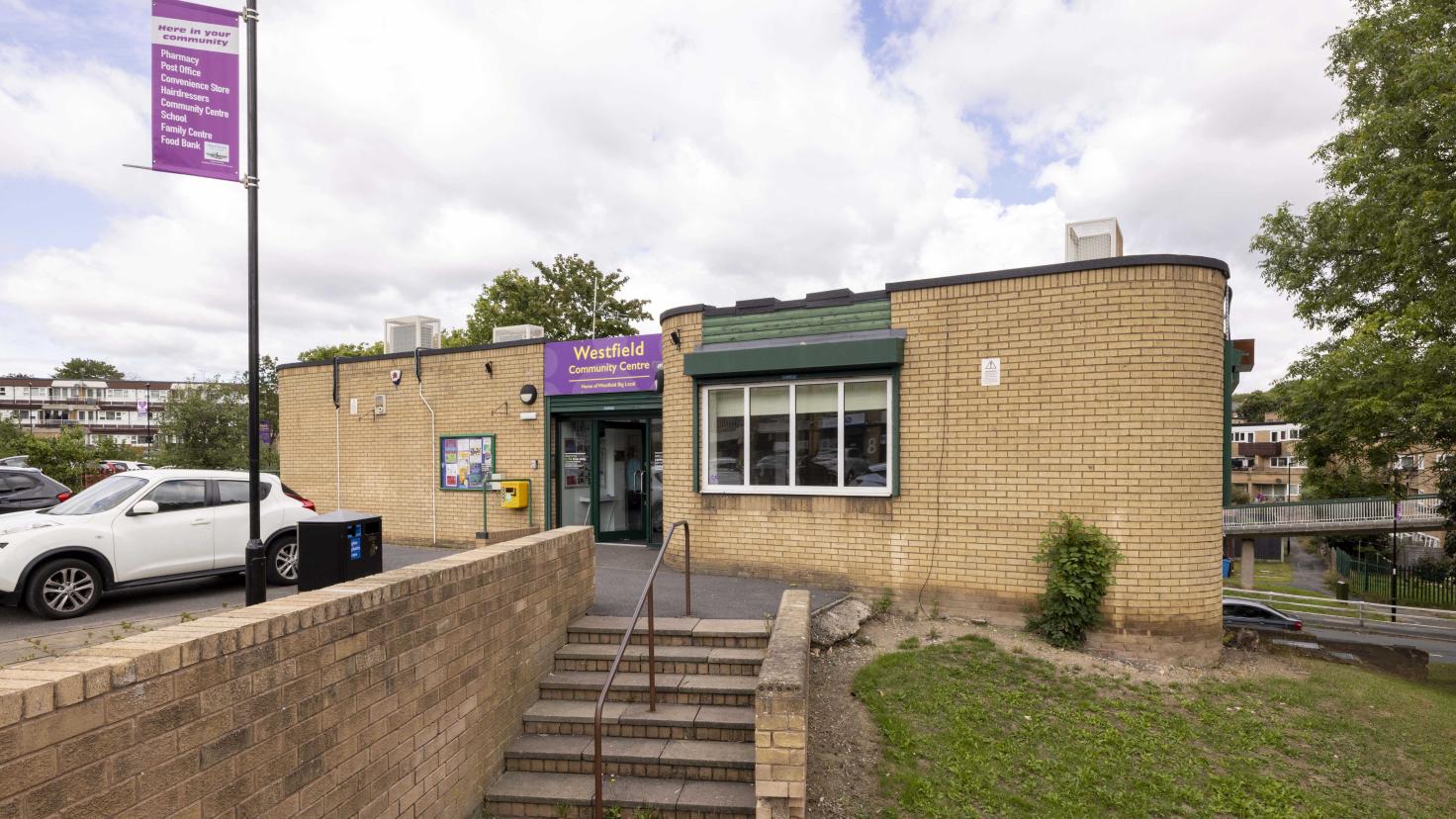One-storey yellow bricked building with steps outside and a purple sign reading 'Westfield Community Centre'