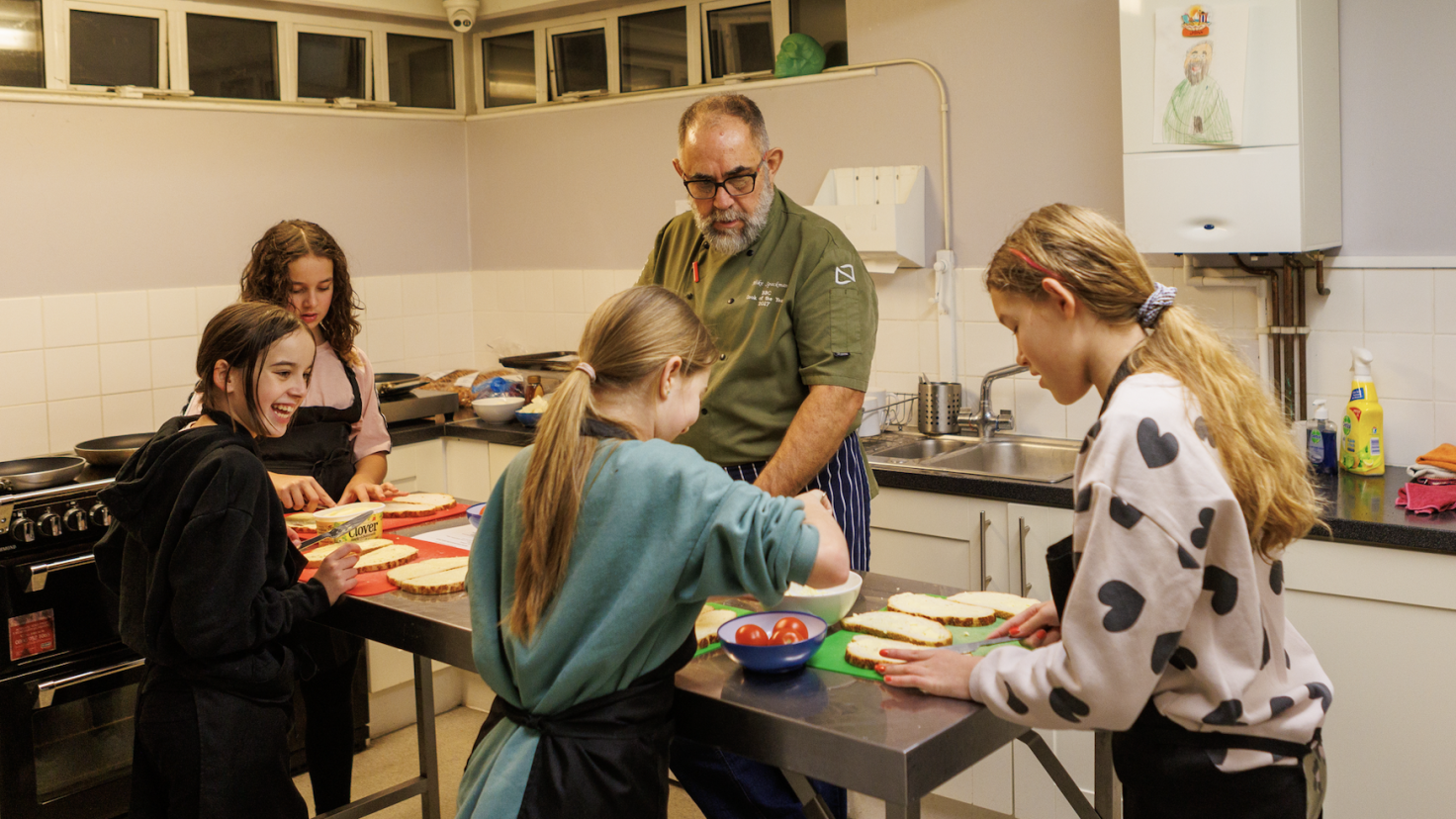 Four young people and an adult making food on a table in a kitchen