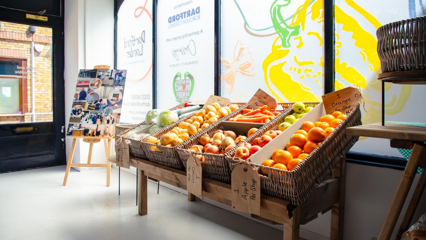 Vegetable racks by a sunny shop window, displaying colourful fruit.
