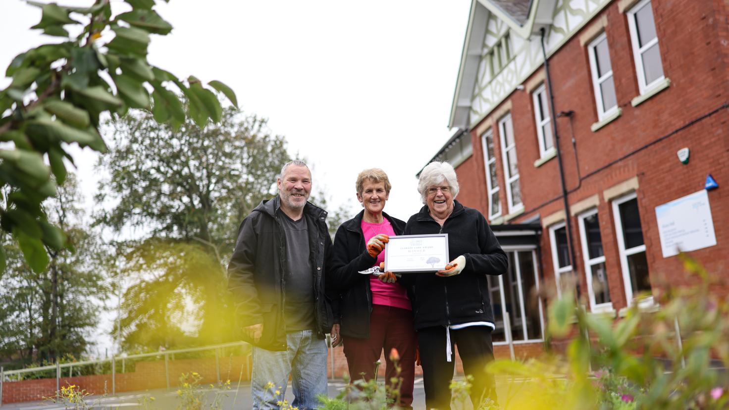 Three people stand over a well-planted border and smiling at the camera.