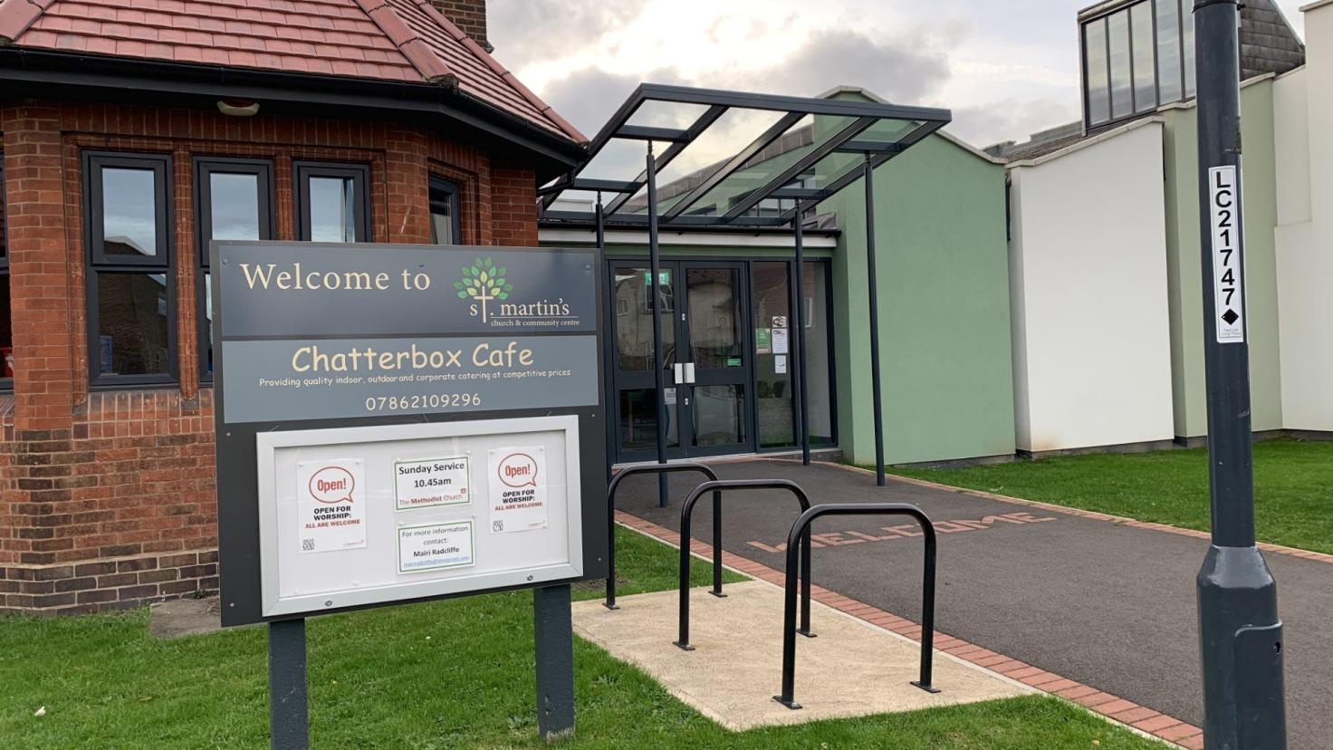 A single-storey red-brick building behind a sign reading 'Welcome to Chatterbox Cafe'.