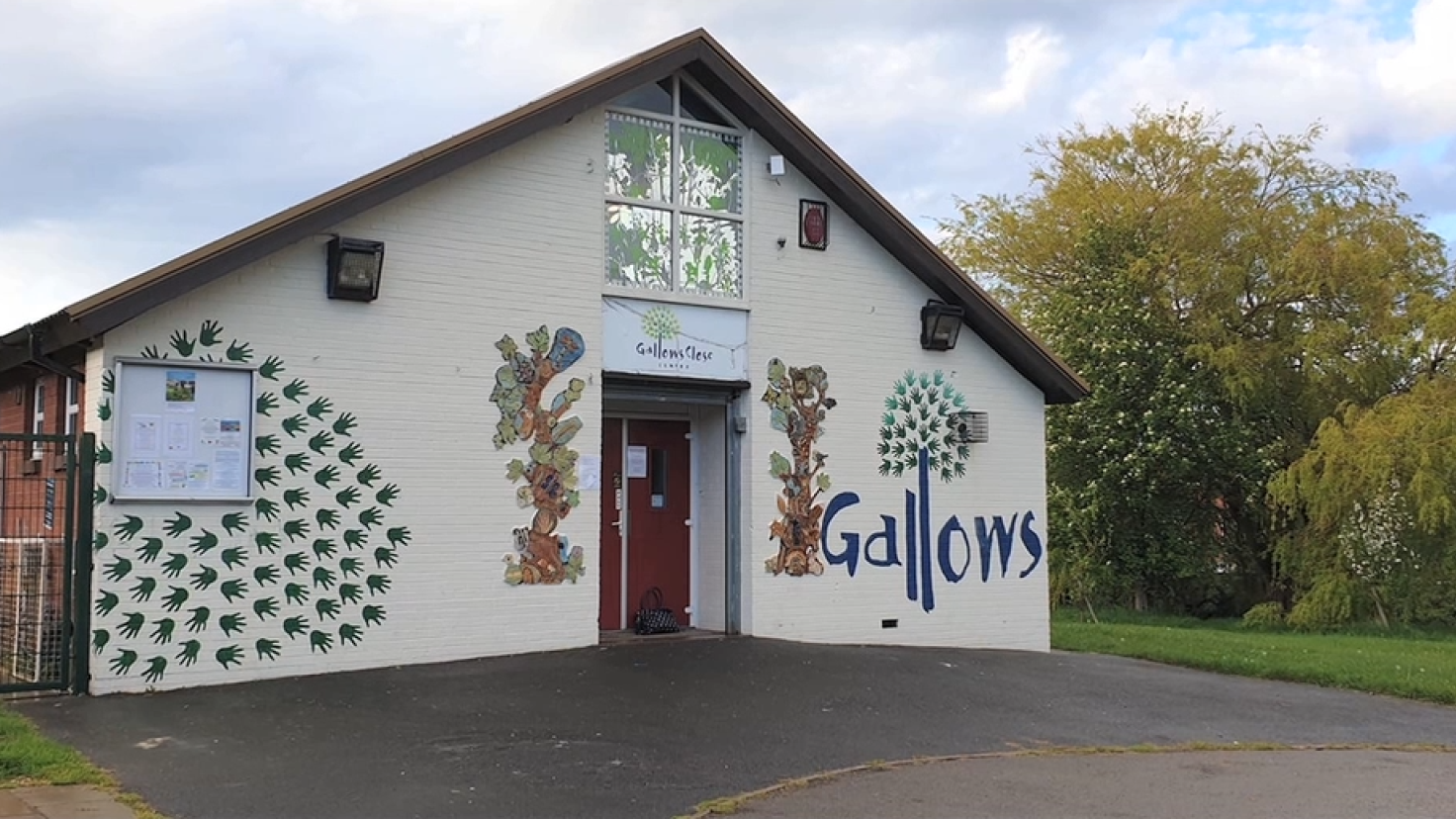 A single-storey community centre with trees behind, with murals and the word 'Gallows' painted on the front elevation.