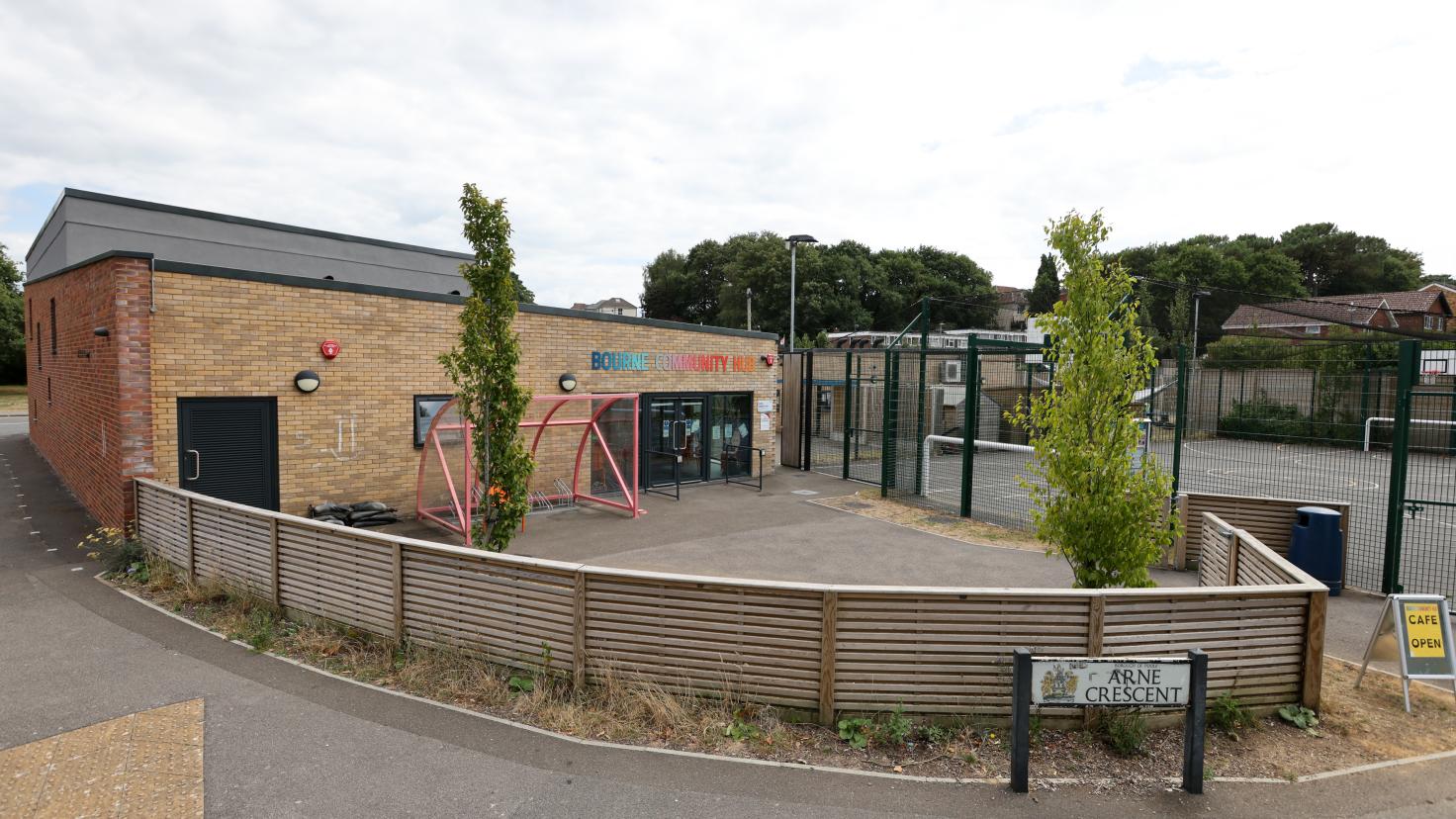 A single-storey brick building with a fenced yard to one side, containing two trees and a bike shelter.