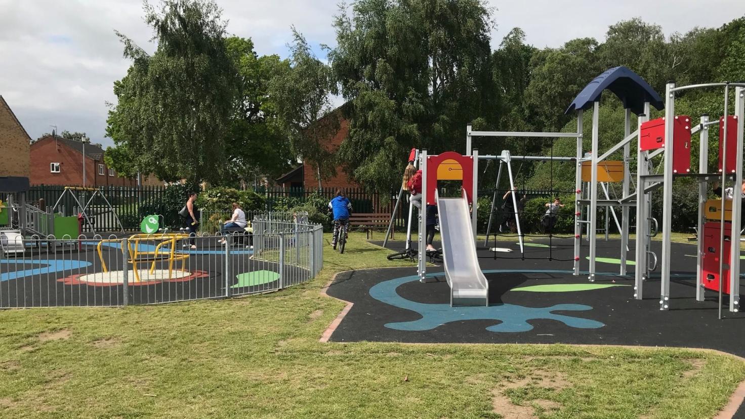 A play park with a grassy area and large colourful climbing frames, a roundabout and a slide.