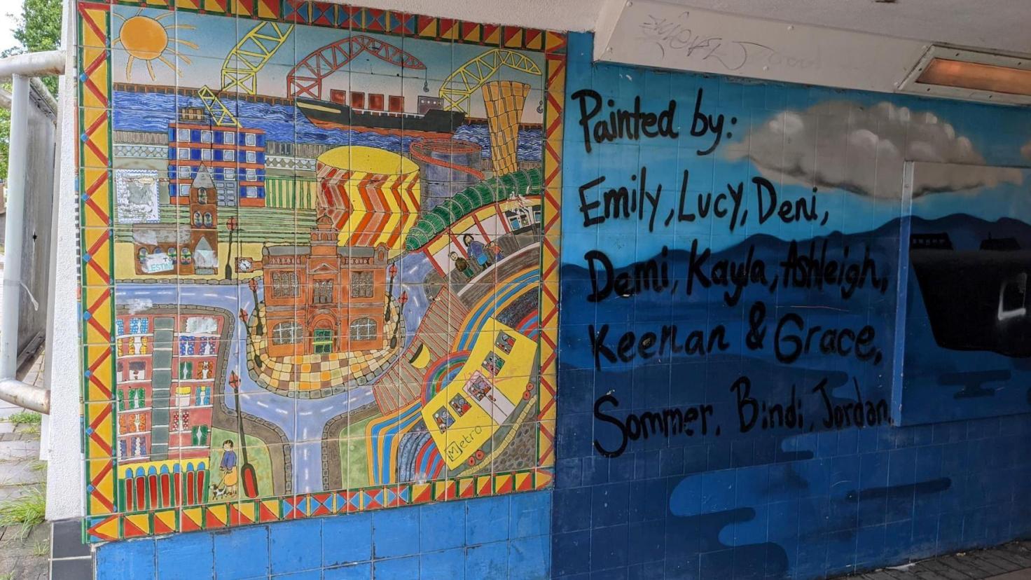 A colourful tiled mural in an underpass showing a street scene and a port.