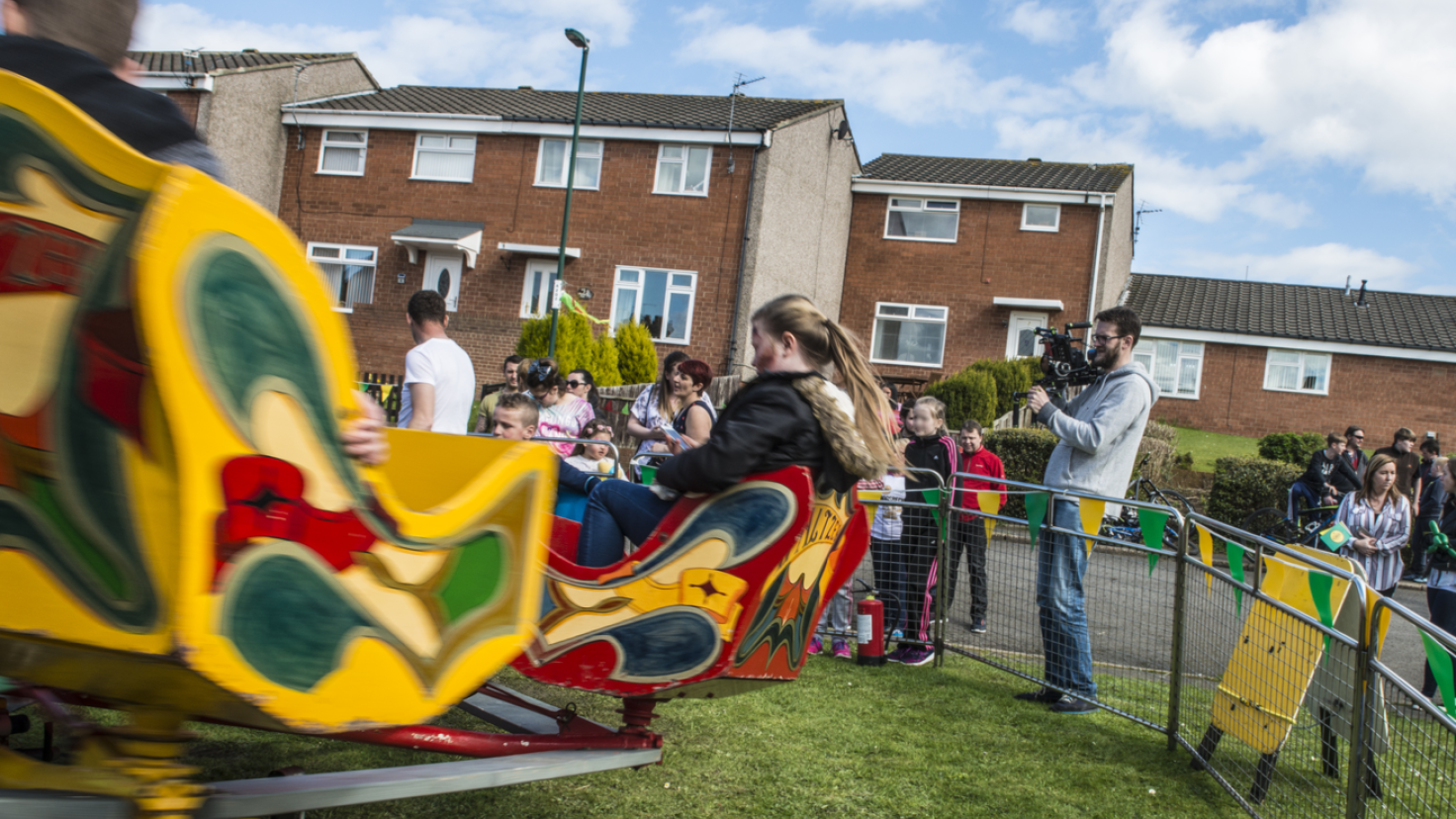 Funfair rides in motion in front of red-brick housing.