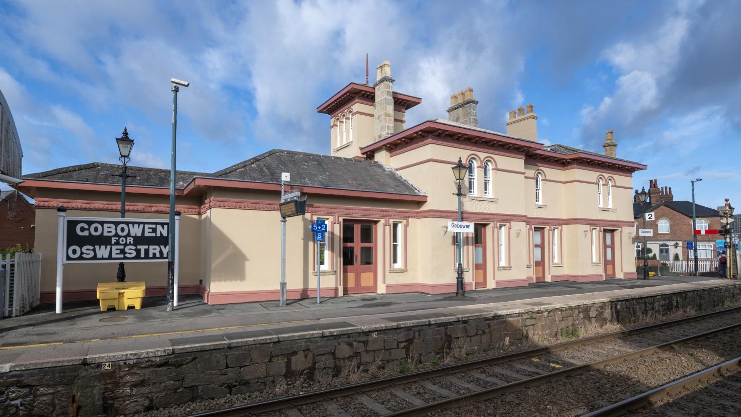 A peach coloured building of one and two-storeys situated on a concrete platform with a sign reading 'Gobowen for Oswestry'