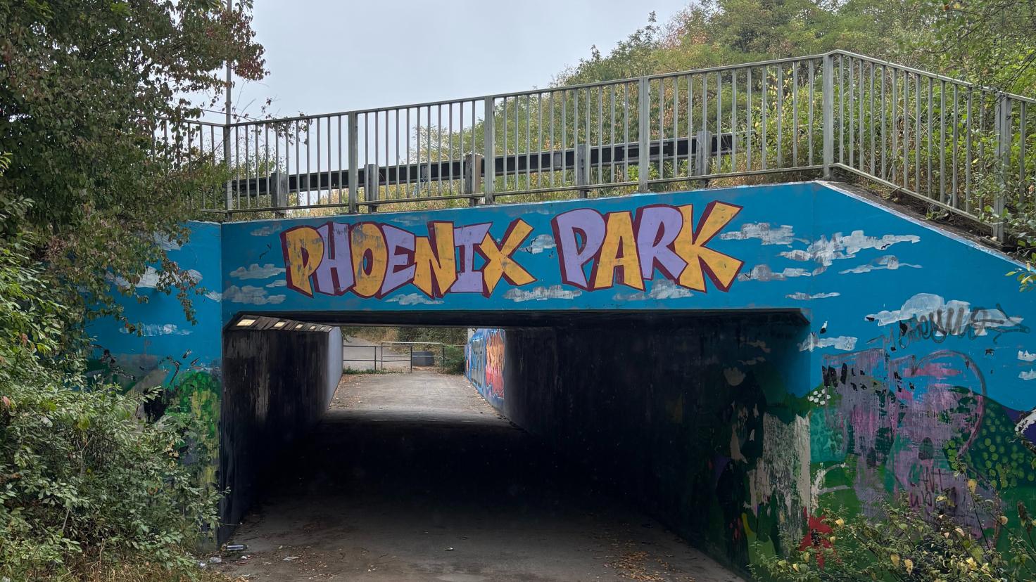 Pathway under a painted blue bridge with writing reading 'Phoenix Park'