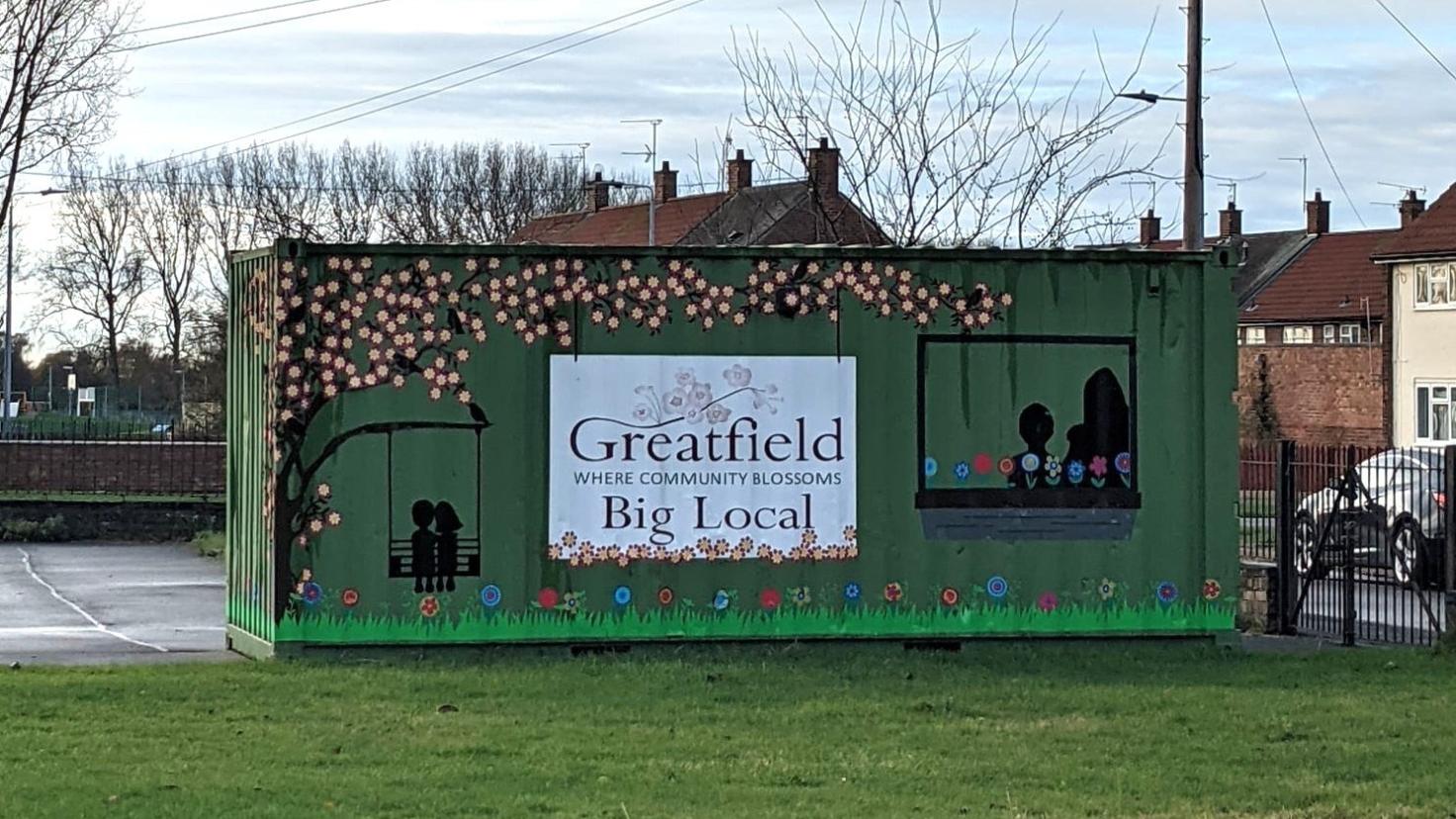 A green shipping container painted with a colourful mural and the sign "Greatfield Big Local".