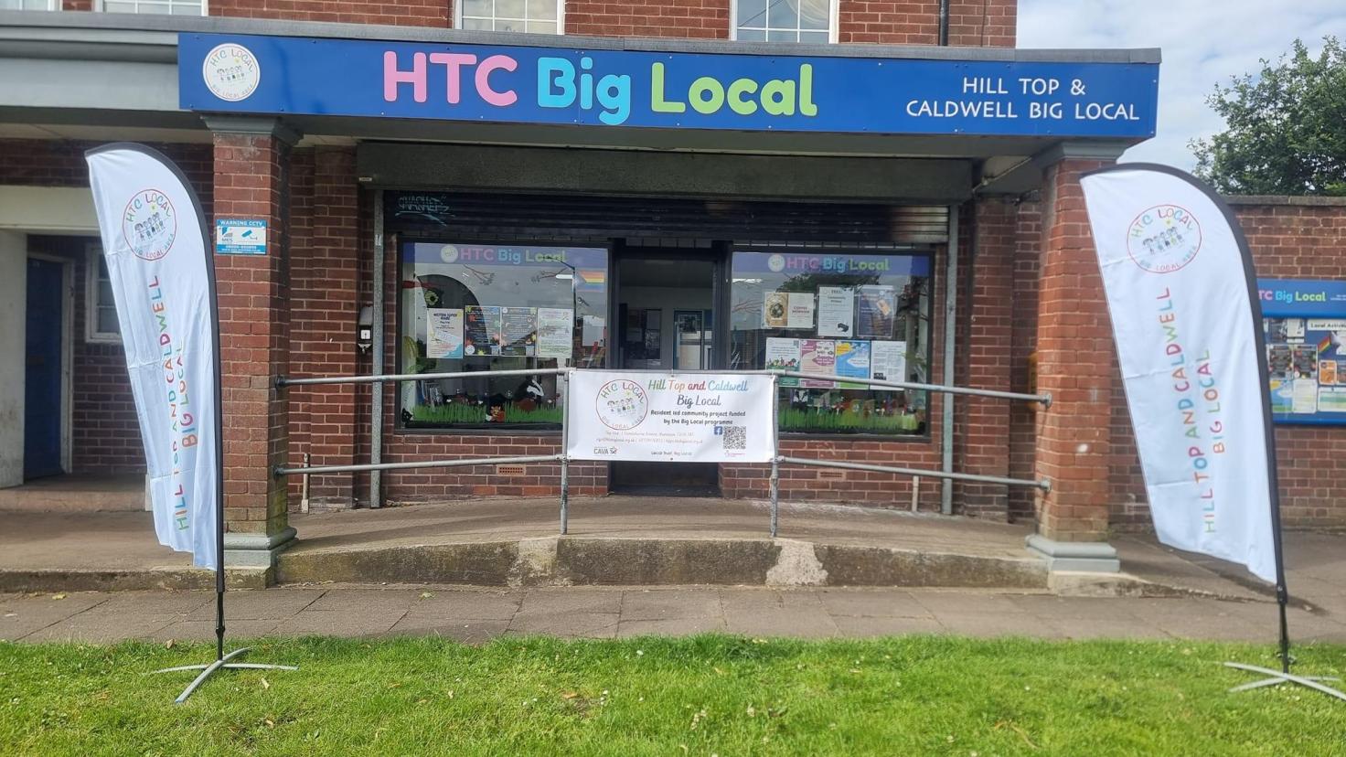 Shop front flanked by banners with a sign reading 'HTC Big Local' above the shop.