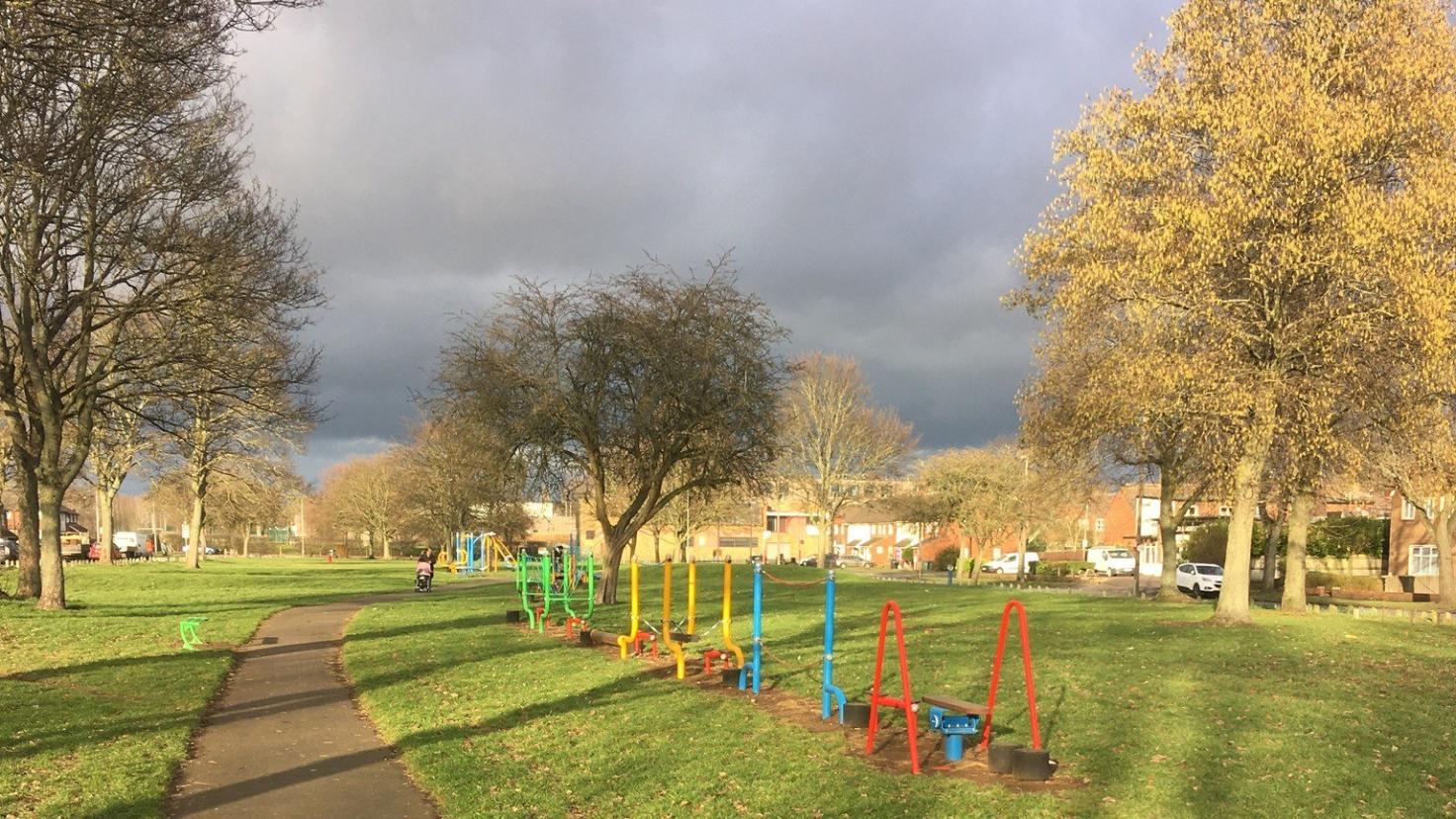 A path running through a green parkland with trees and play equipment.
