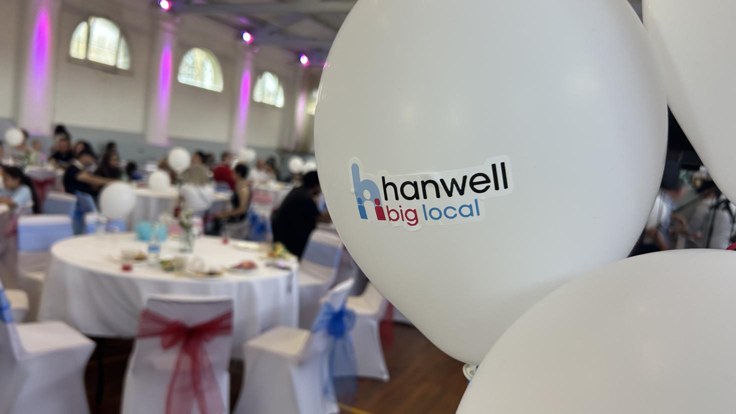 White balloons saying Hanwell Big Local with tables and chairs in the background decorated for a formal event.