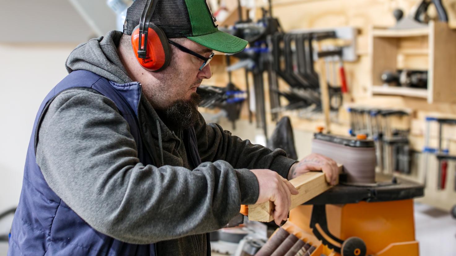 A man wearing ear defenders doing wood work with a block of wood and a machine