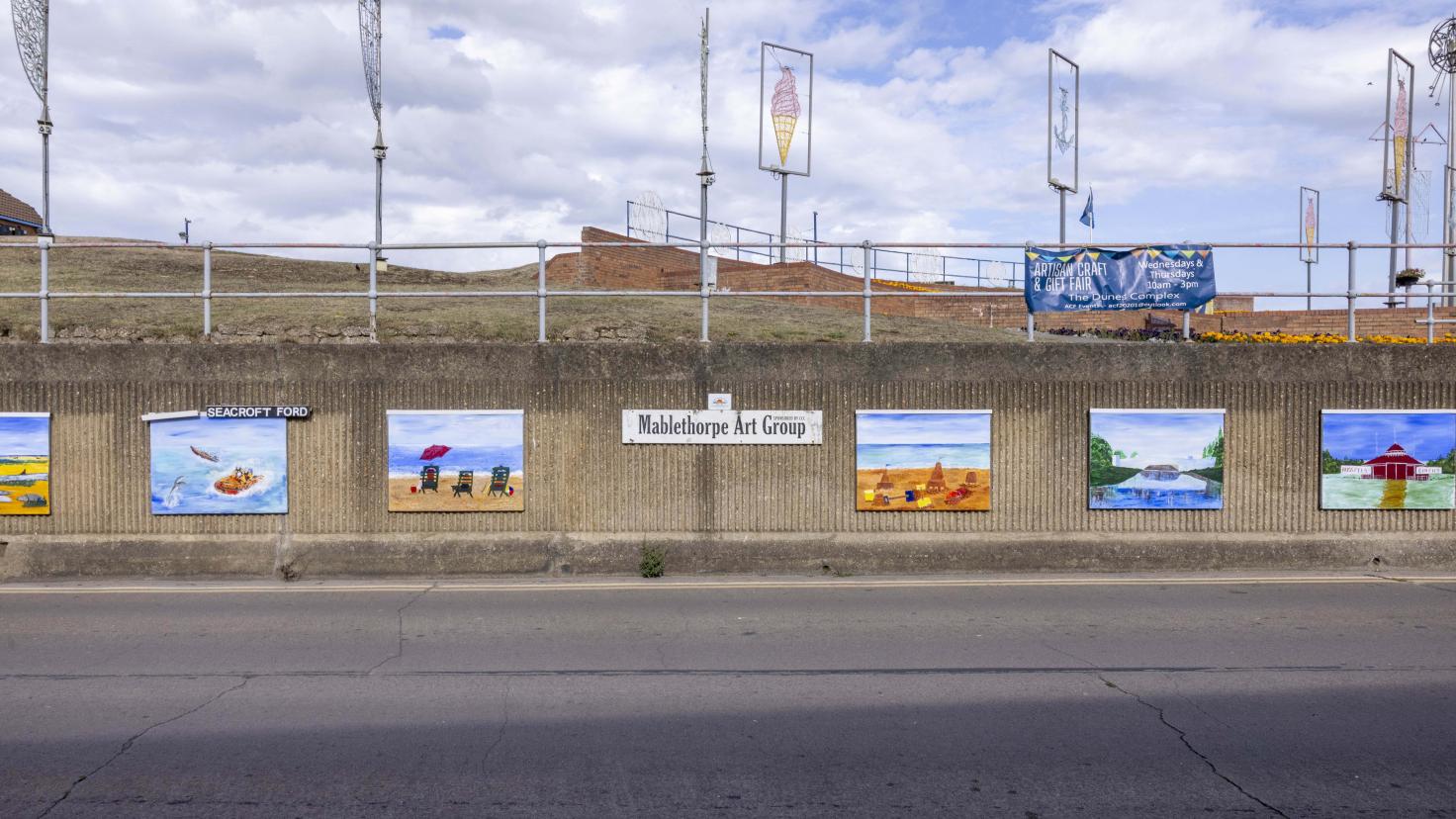 A concrete wall with mounted colourful rectangular paintings and a sign reading 'Mablethorpe Art Group'.