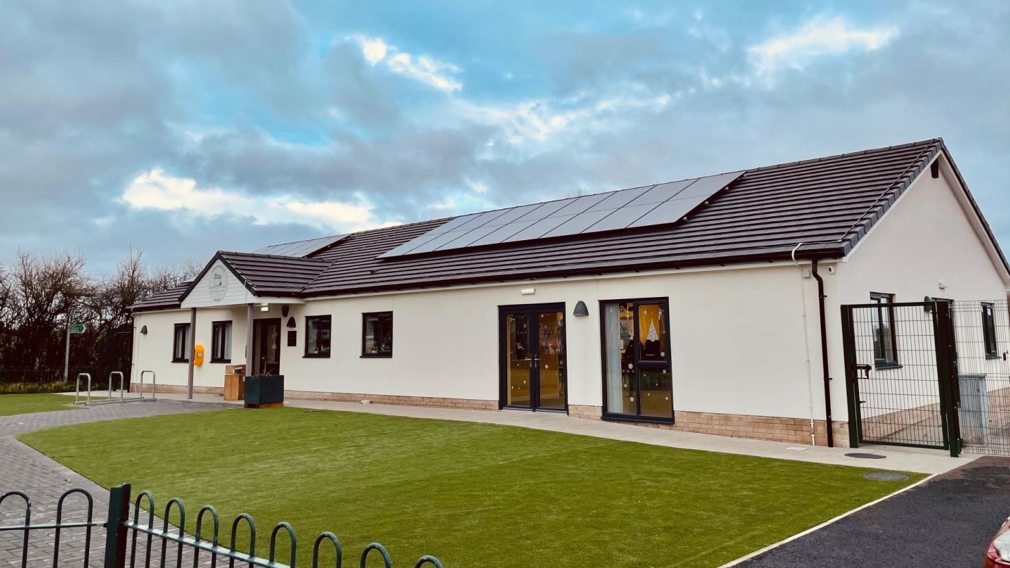 A single storey building with cream walls and a solar panel on the roof, with a lawned area in front.