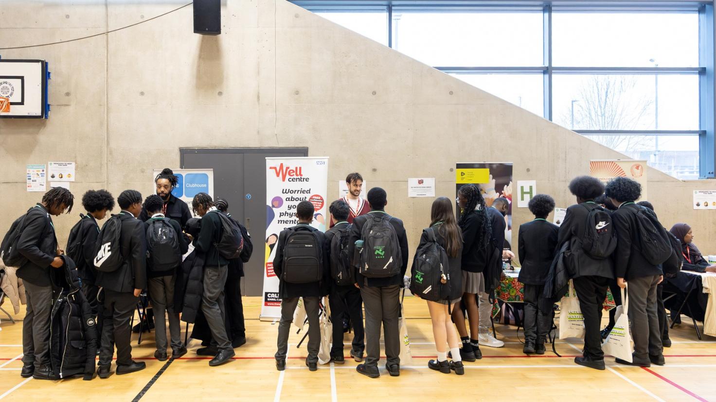 Young people in a hall, gathered around tables and displays.