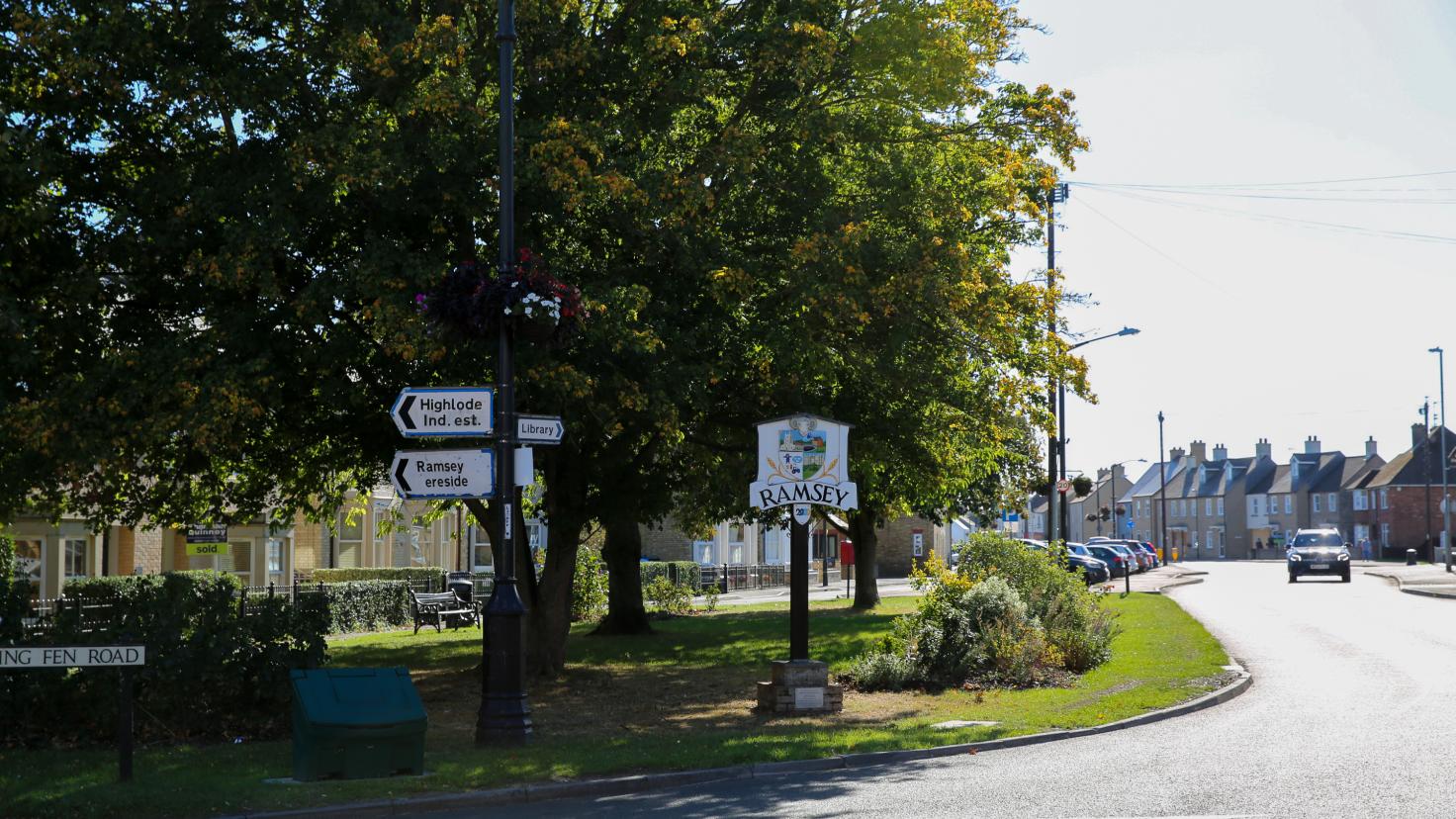 Green space with trees and a tarmacked road and a sign that reads Ramsey