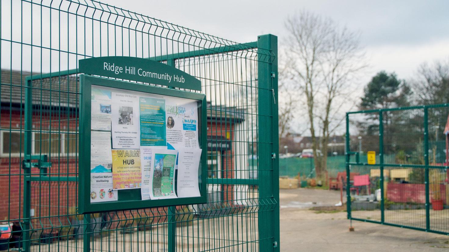 Noticeboard on green fencing reading 'Ridge Hill Community Hub' and posters advertising activities at the hub