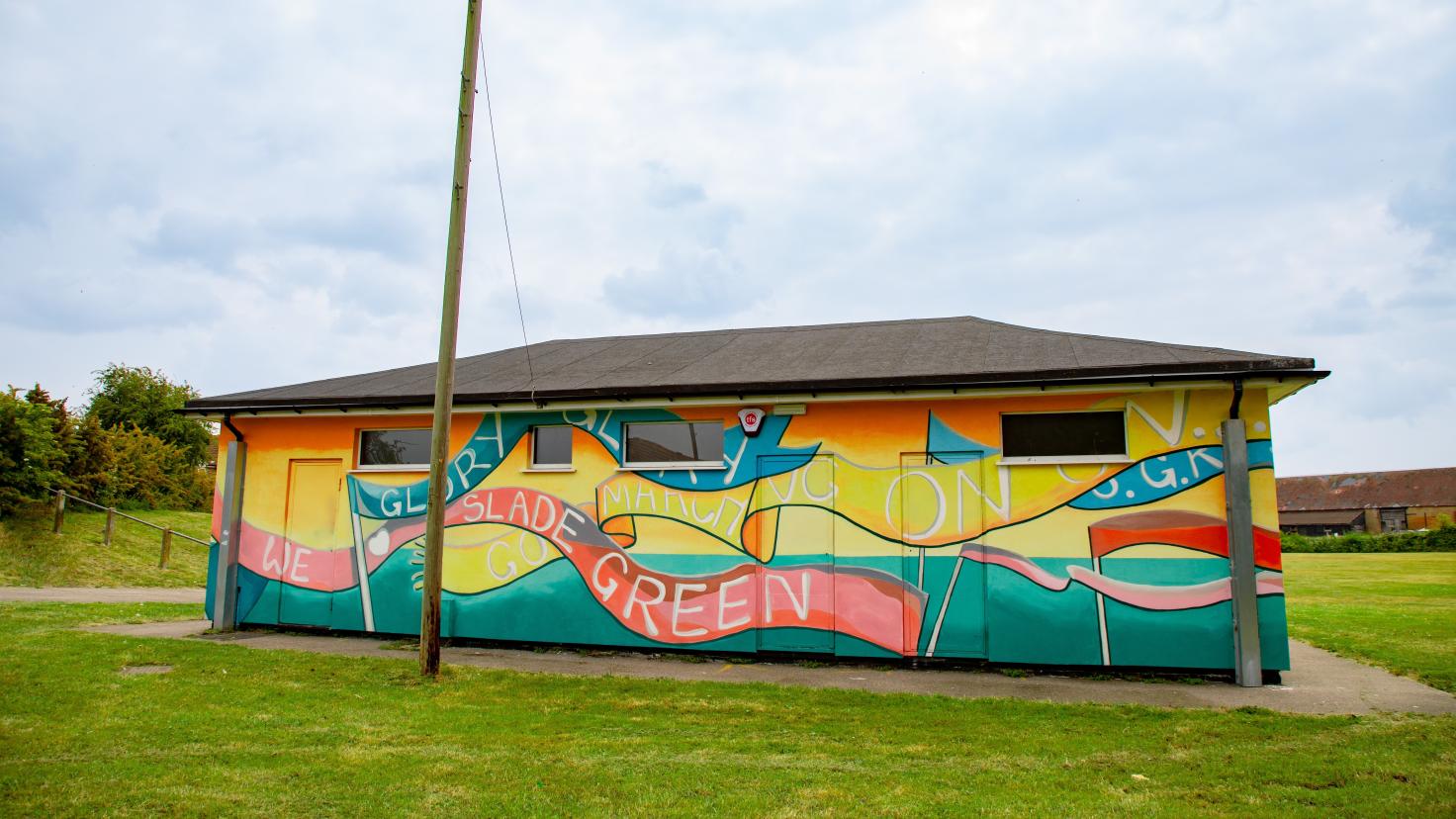 One-storey building painted yellow and turquoise green with a red banner reading 'Slade Green'