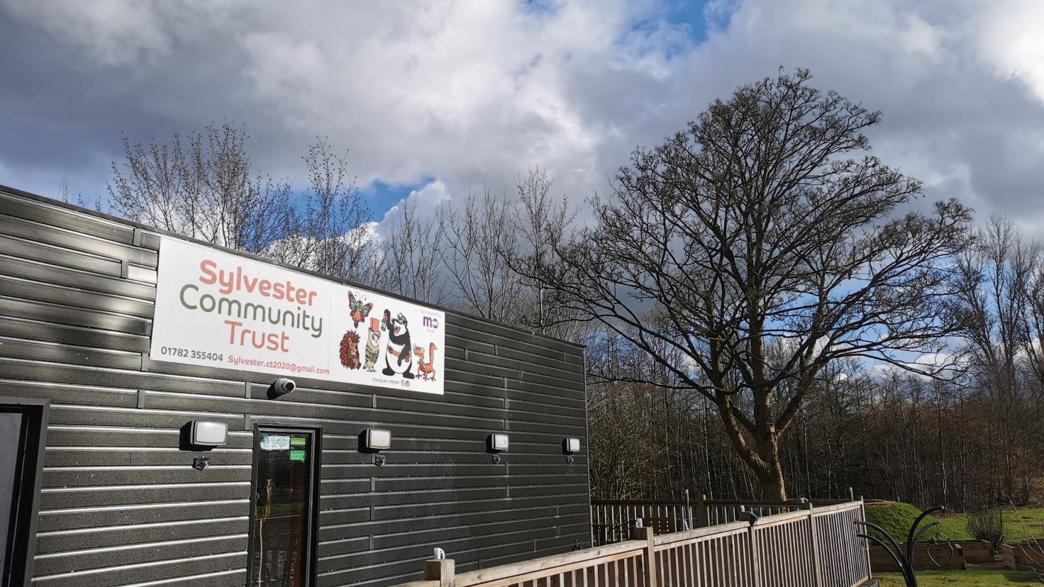 A single-storey building behind railings, with a banner reading 'Sylvester Community Trust'.