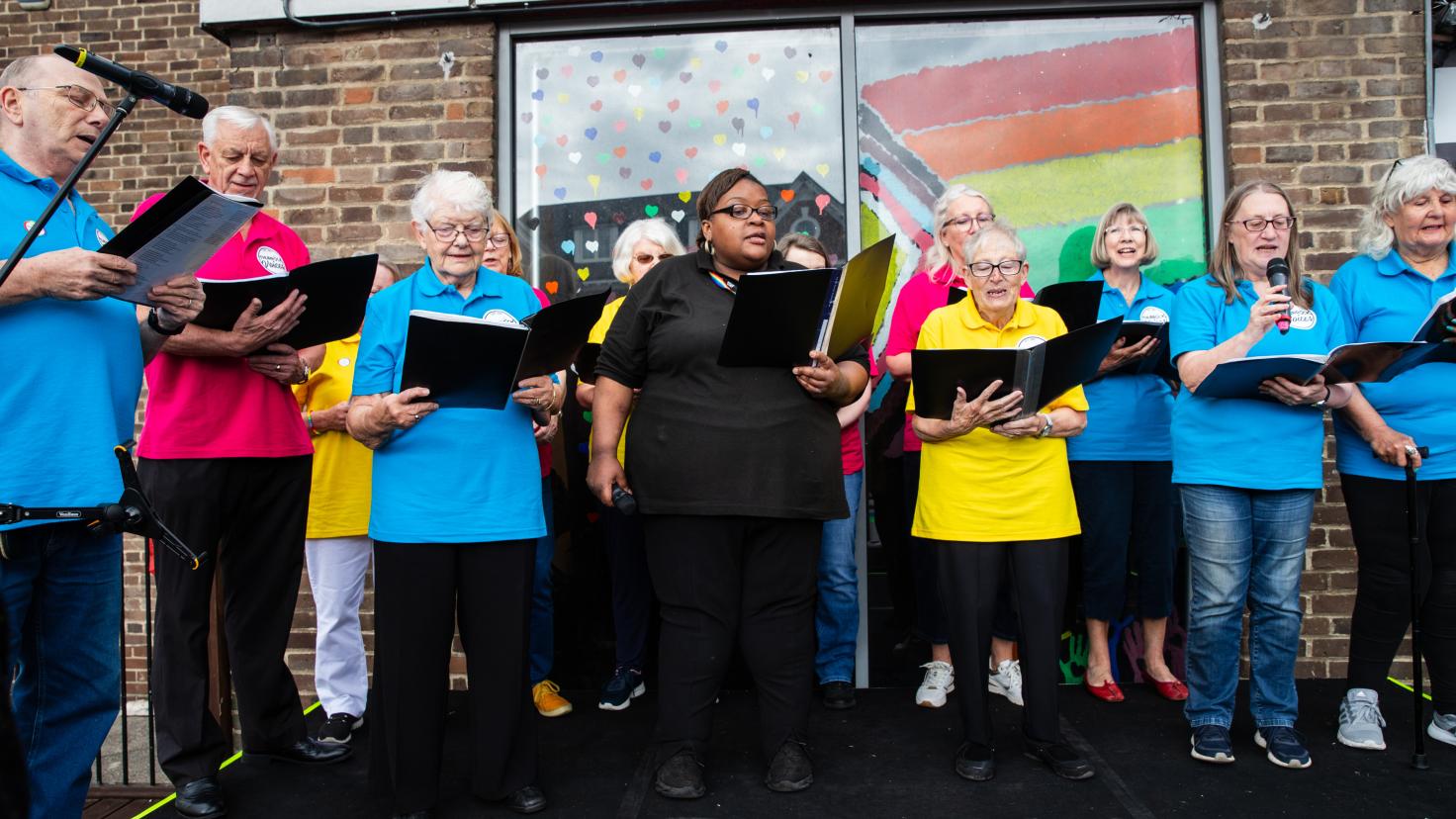 A choir in colourful polo shirts singing, with each person holding an open music folder.