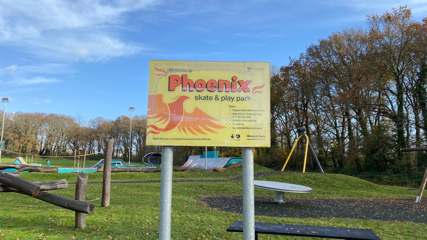 A sign reading 'Phoenix' in front of a play park and a bench.