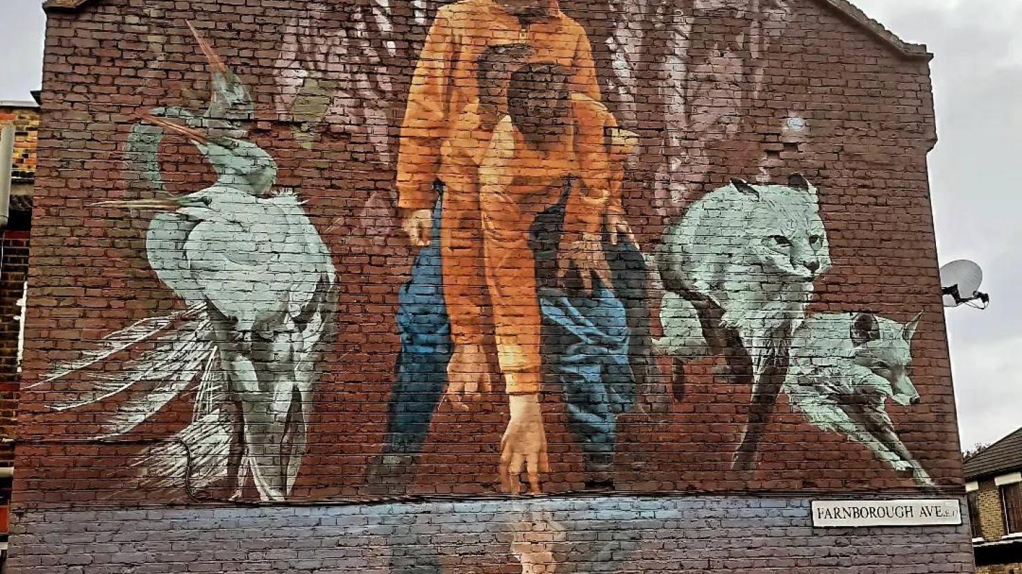 A mural covering the side of a red-brick building depicting a young person bending down towards a reflecting pool.