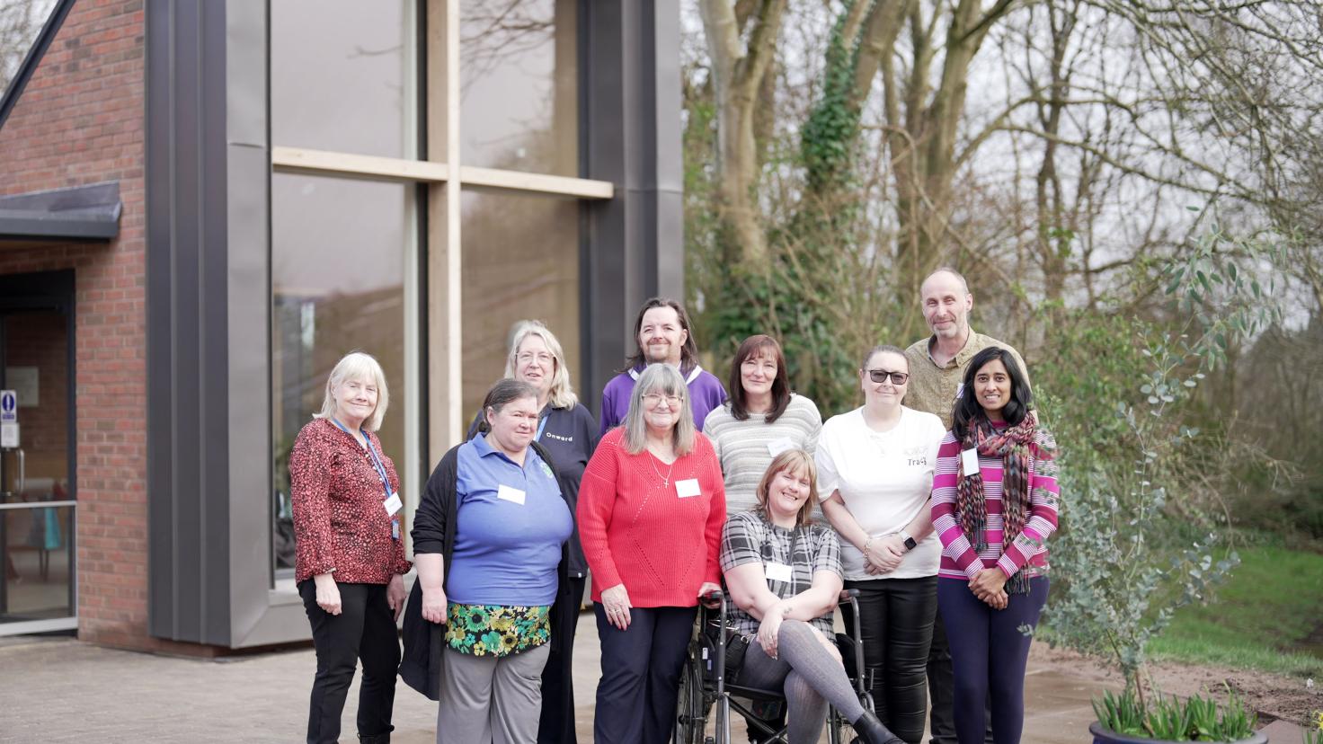 A group of people smiling at the camera outside a modern red-brick building with large windows.