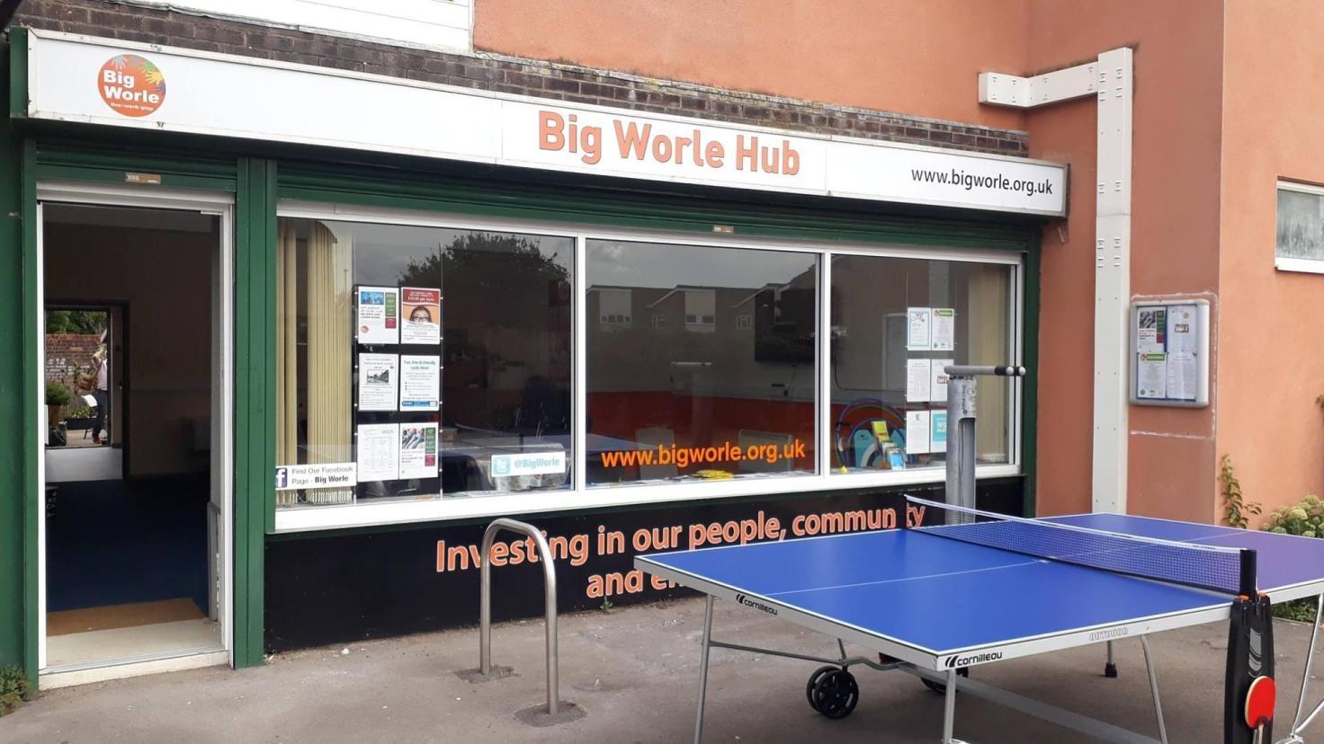 A single-storey shop front below a sign reading 'Big Worle Hub', with a table-tennis table in front of the building.