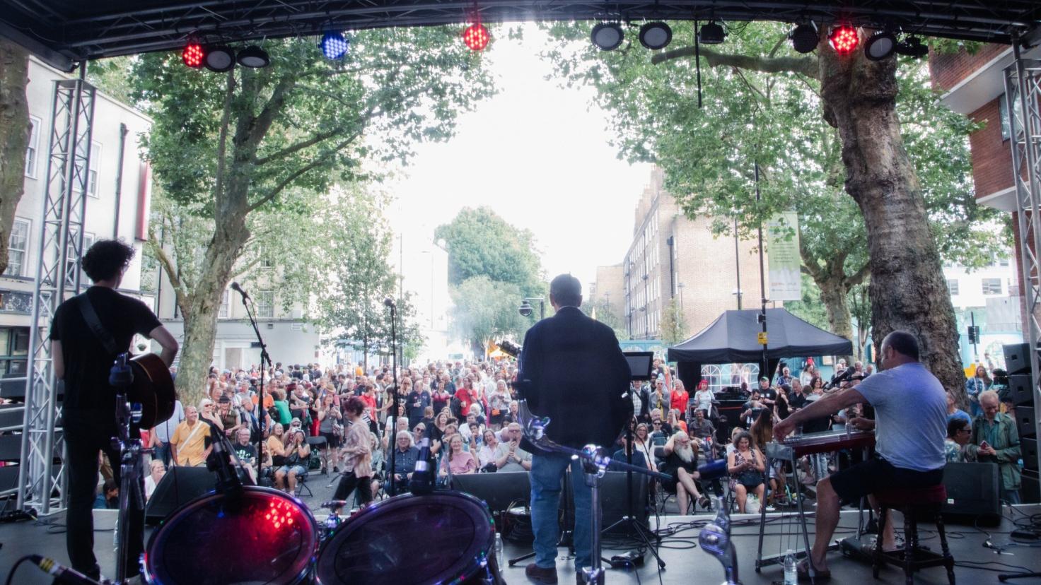 A photo of a large crowd taken from behind the members of a band on an outside stage.