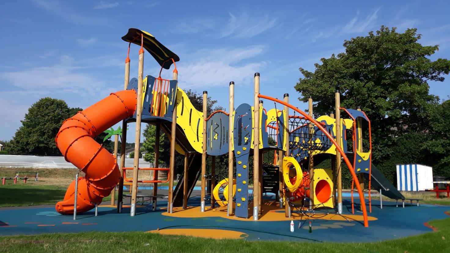 A sunny play area with huge colourful play equipment including a bright orange covered slide.