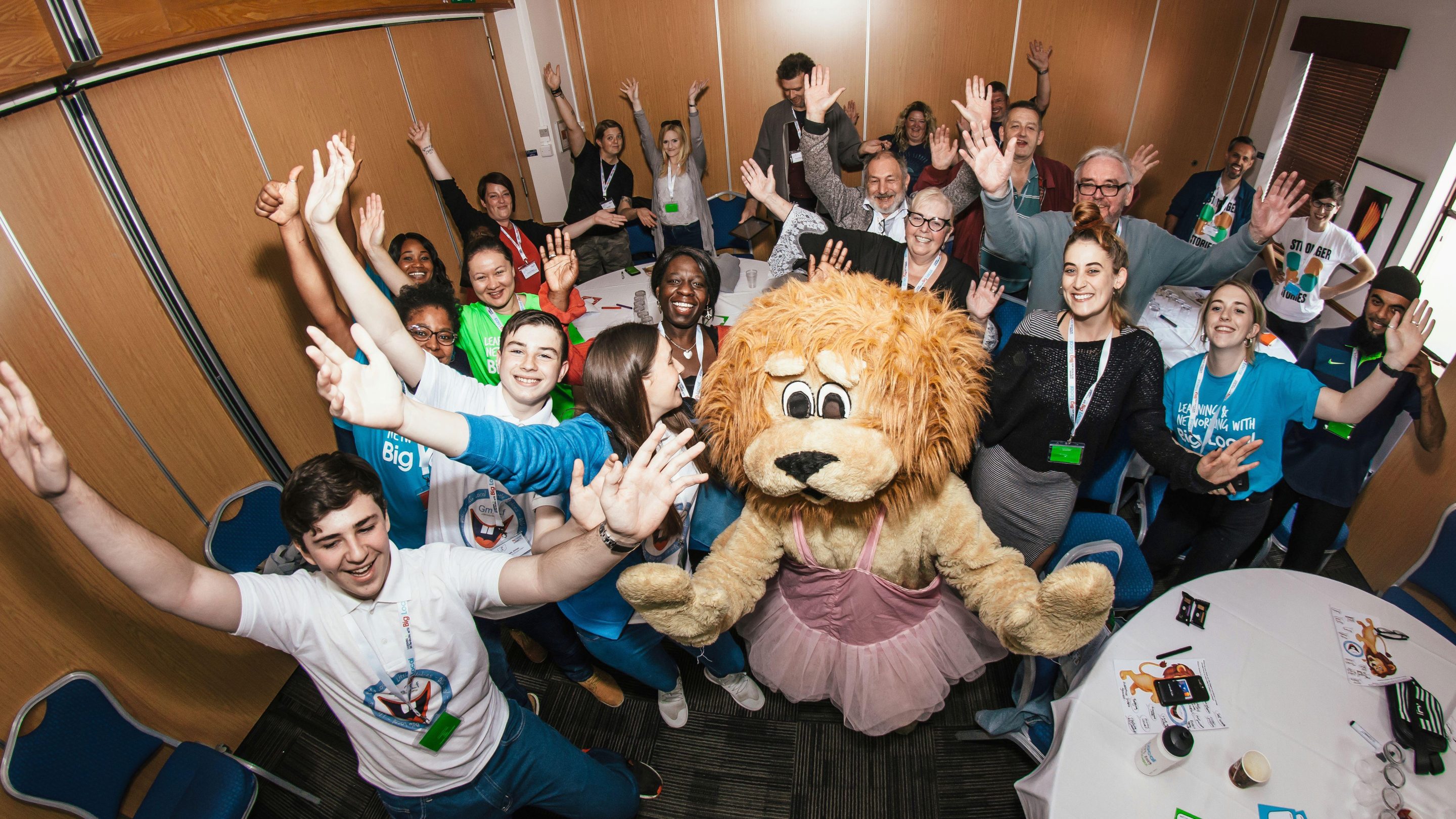 A group of young people with their hands in the air and a person wearing a lion costume and a tutu.