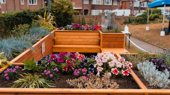 A wooden seating area, planted with flowers, with houses in the distance.
