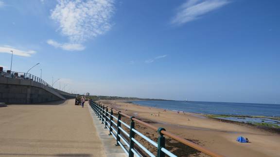 A view of the seafront promenade and sandy beach at low tide, on a sunny day with clear blue skies.