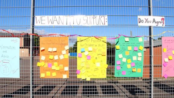 Brightly-coloured posters covered in post-in notes, attached to a steel mesh fence.