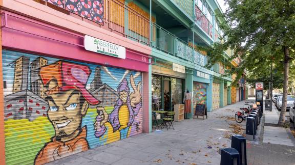 A row of colourful high street shops with spray-art murals on the front of the nearest shop.