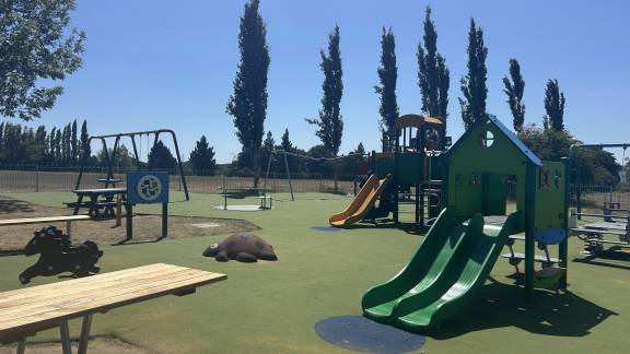 Play equipment including slides and swings on a grassed area, with picnic tables in the foreground.