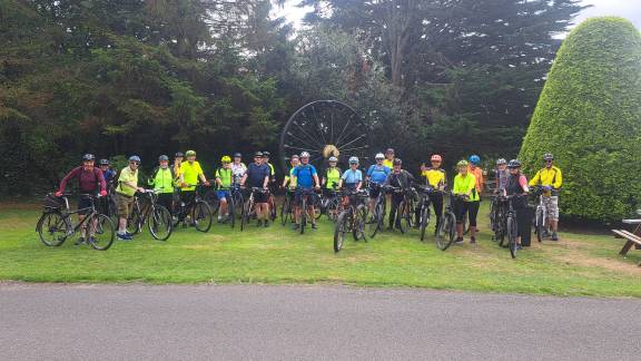 A large group of people in high-vis cycling gear, astride bikes and smiling for the camera.