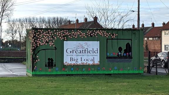 A green shipping container painted with a colourful mural and the sign "Greatfield Big Local".