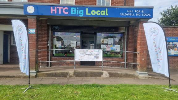 Shop front flanked by banners with a sign reading 'HTC Big Local' above the shop.