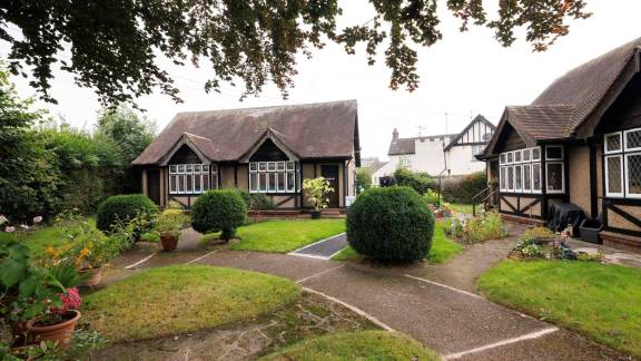 A small gable-fronted mock-Tudor style building on a pretty manicured lawn.