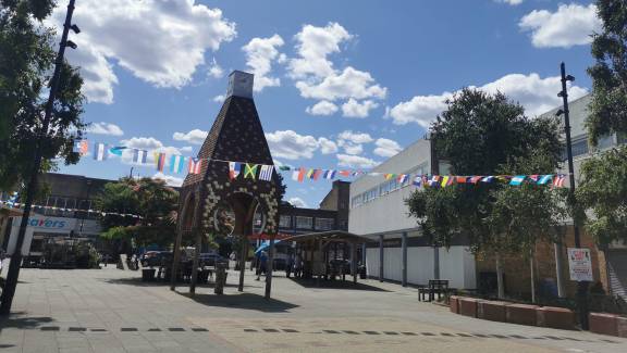 Square outside area with a red brick clock tower structure and world flag bunting hanging from two posts