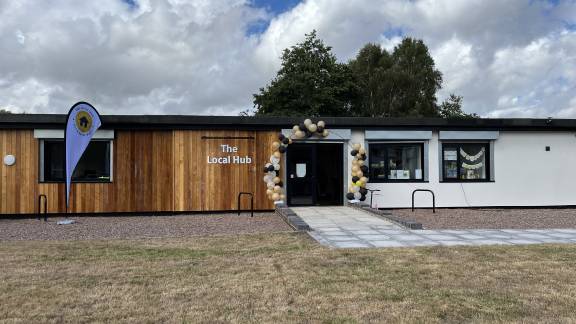 A single-storey modern building with cedar cladding and large windows, and a balloon arch over the door.