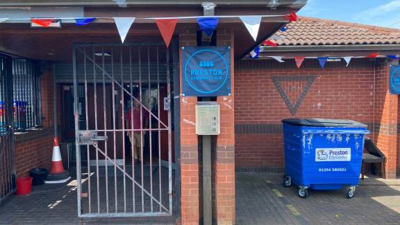 Red brick building with a grey gate and Preston Community Hub sign