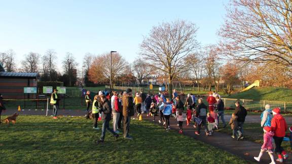 A group of people of mixed ages running through a park.